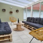 Grande véranda donnant sur le jardin avec 2 banquettes en palettes, 2 fauteuils et table de salon. Livre et jeux de société Grande véranda donnant sur le jardin avec 2 banquettes en palettes, 2 fauteuils et table de salon. Livre et jeux de société