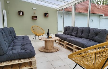 G&icirc;te n&deg;G622534 Saint-Martin-Boulogne - Pas-de-Calais - Grande v&eacute;randa donnant sur le jardin avec 2 banquettes en palettes, 2 fauteuils et table de salon. Livre et jeux de soci&eacute;t&eacute;